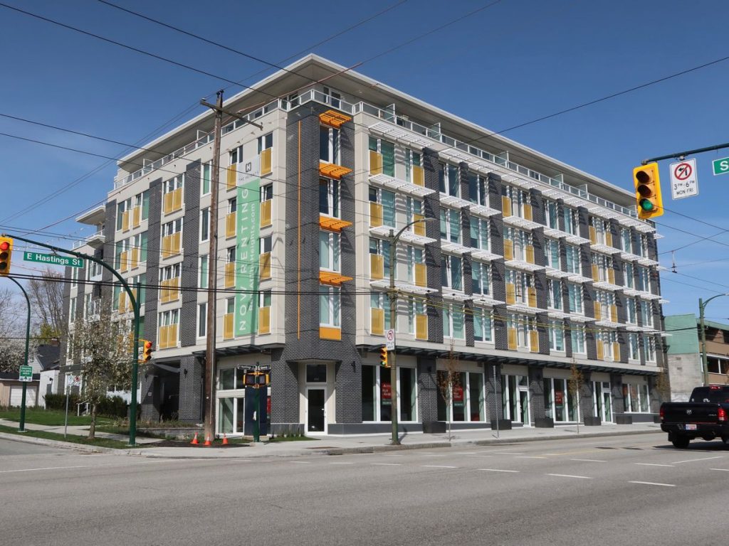 Six story gray building with yellow accents on street corner