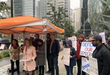 Subscriber Drive: Summer Stinson Testimonial Speakers gather under an umbrella as supporters hold signs behind