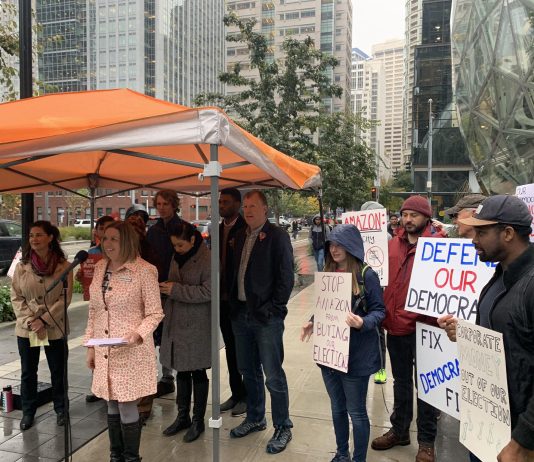 Subscriber Drive: Summer Stinson Testimonial Speakers gather under an umbrella as supporters hold signs behind
