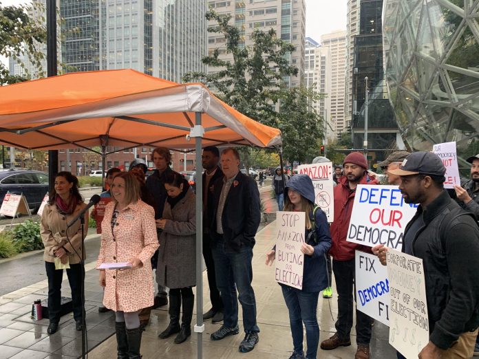 Speakers gather under an umbrella as supporters hold signs behind