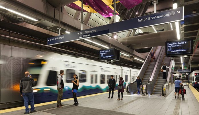 An underground light rail station with a train and passengers.