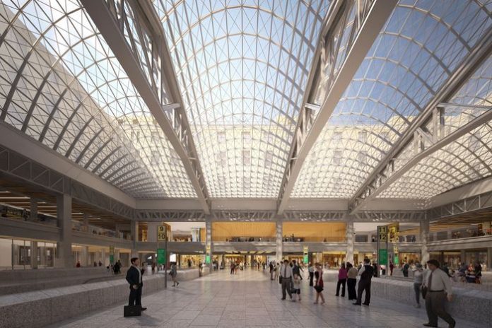 An airy train station with a glass ceiling held by steel latticework.