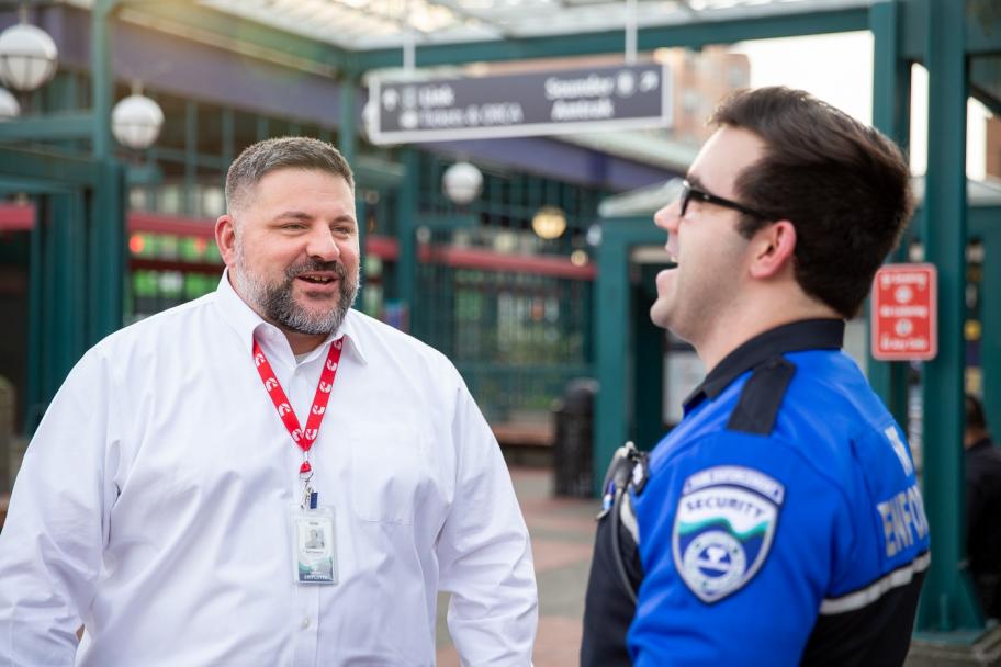 A fare enforcement officer in a blue and black uniform talks to a Sound Transit employee.