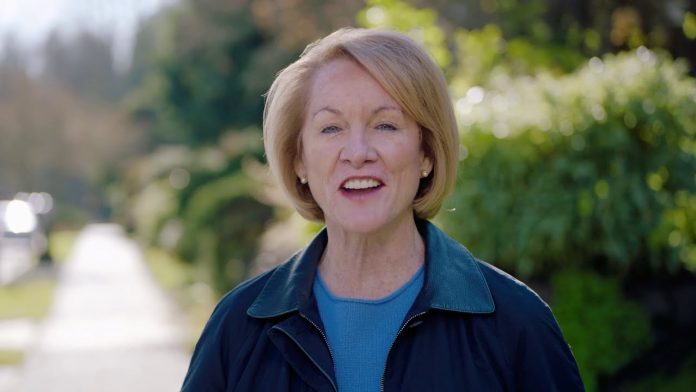 Mayor Durkan stands on a sidewalk on a leafy residential block.