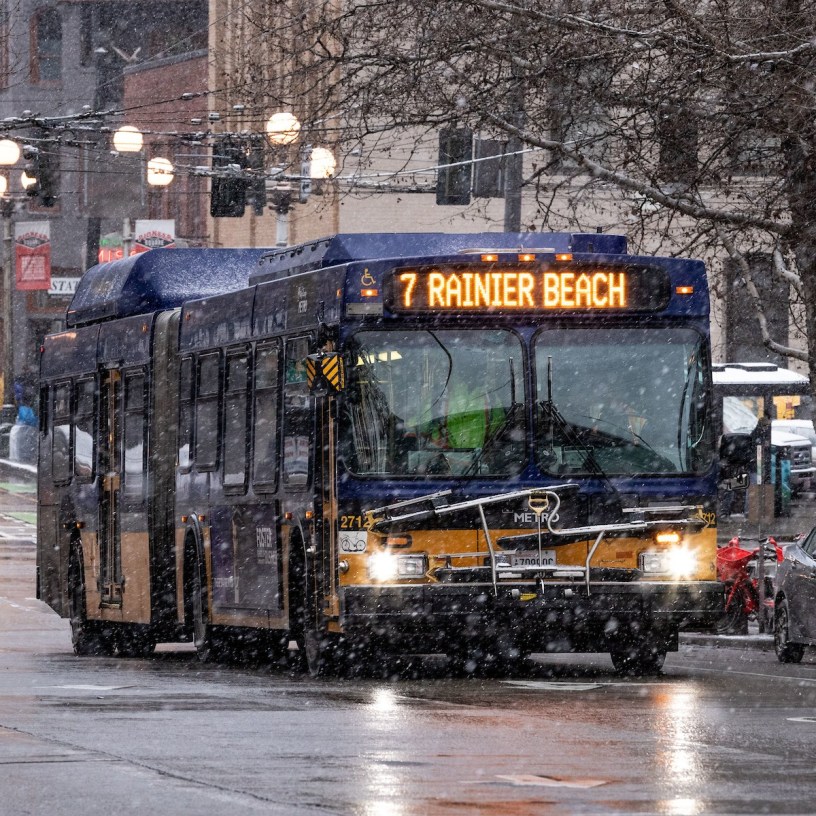 Route 7 bus driving down the street with some light snow coming down.