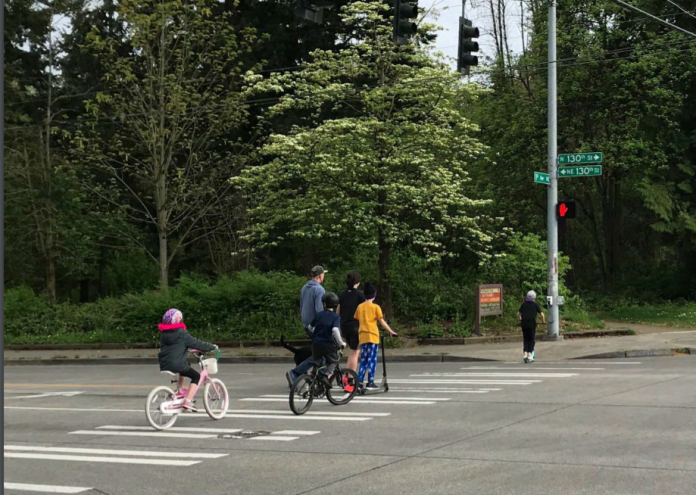 A family on bikes crosses a 130th Street crosswalk.