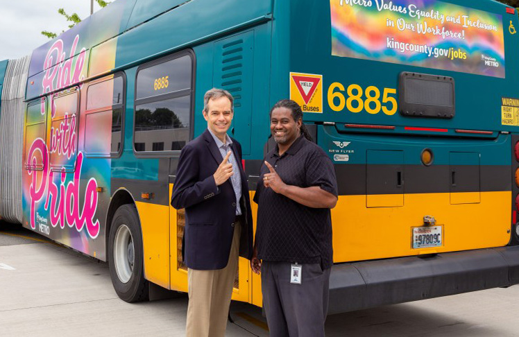 A Metro bus with a rainbow Pride wrap is the backdrop for Metro executives Rob Gannon and White.