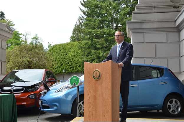 Governor Jay Inslee at a podium with two electric cars behind him.