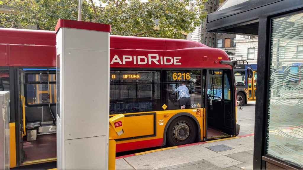A red RapidRide bus at a stop with a off-board payment kiosk and bus shelter.
