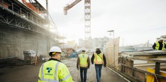 Three construction workers in Sound Transit vests walk a construction site with crane overhead.