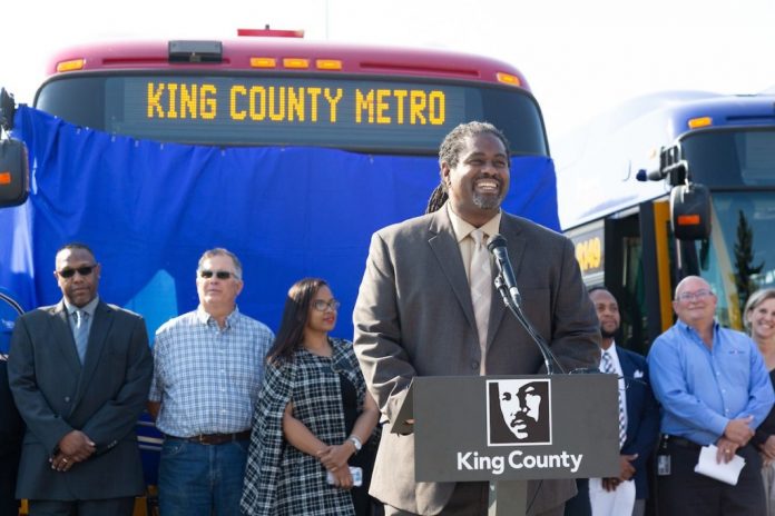 Terry White at a podium in front of a Metro bus flanked by Metro coworkers at a 2018 event.