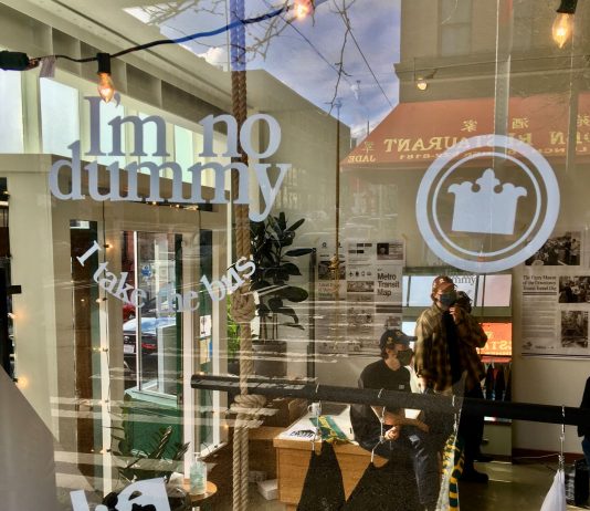 The New Bootleg Brand Uncovering the Best of Seattle’s Historic Iconography Chinatown street reflects in the window of the popup store where Nate and Ryan lean on a counter near their merch.