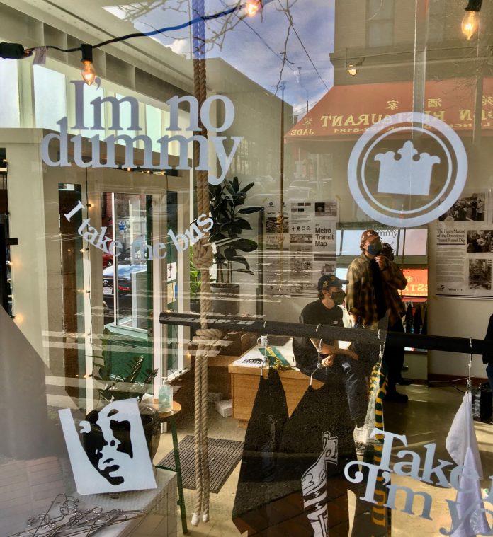 SDoD by Nathan Bombardier Chinatown street reflects in the window of the popup store where Nate and Ryan lean on a counter near their merch.