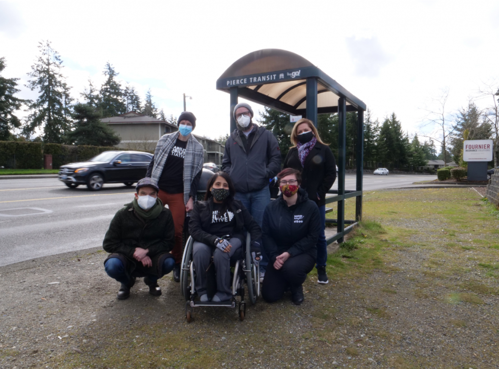 A woman in a wheelchair and five other advocates at a Tacoma bus stop.