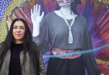 Colleen Echohawk Focuses on Housing the Homeless in Seattle Mayoral Run Colleen Echohawk with a colorful mural in the background showing an indigenous with a handprint over her lips.