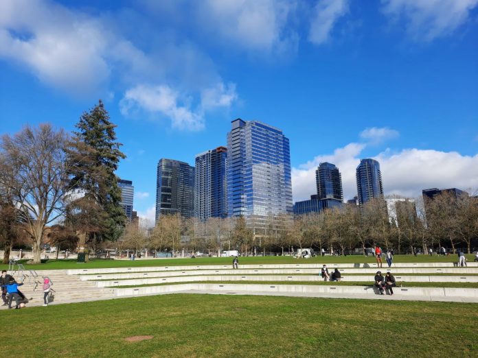 Parkgoes sit on the ampitheater at Bellevue's Downtown park with skyscrapers in the background.