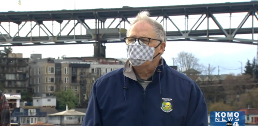 Governor Inslee with a mask speaking in front of I-5 Ship Canal Bridge.