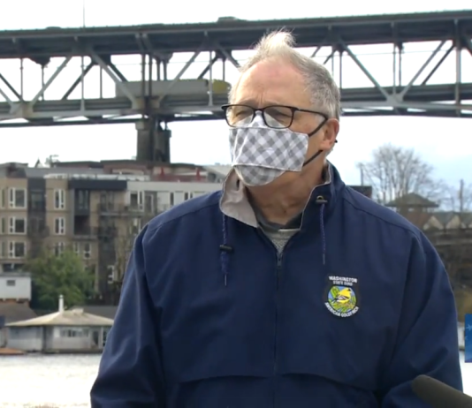 No New Highways Is a 21st Century Imperative Governor Inslee with a mask speaking in front of I-5 Ship Canal Bridge.
