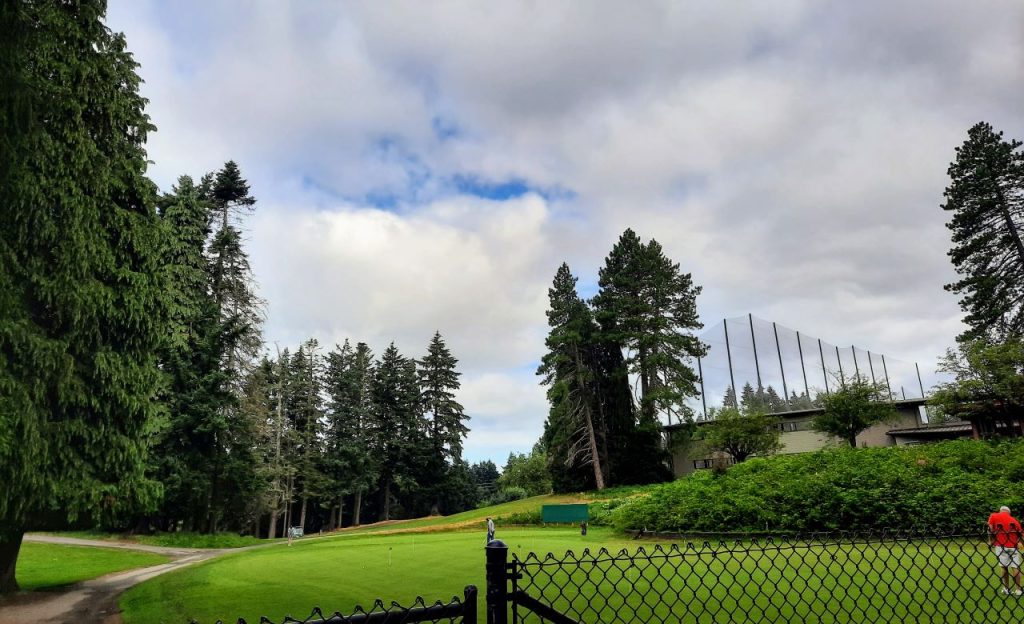 A golf course and driving range with a fence in the foreground.