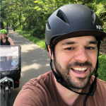 Tom taking a selfie biking on a trail with Kelli and the kid in tow