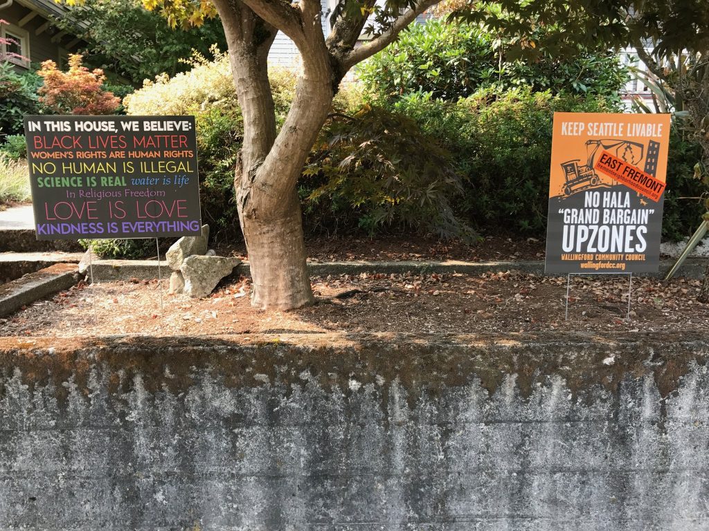 A "in this house, we believe: Black Lives Matter..." sign next to a Wallingford Community Council sign saying "Keep Seattle Livable: No HALA 'Grand Bargain' Upzones" with a East Fremont sticker.