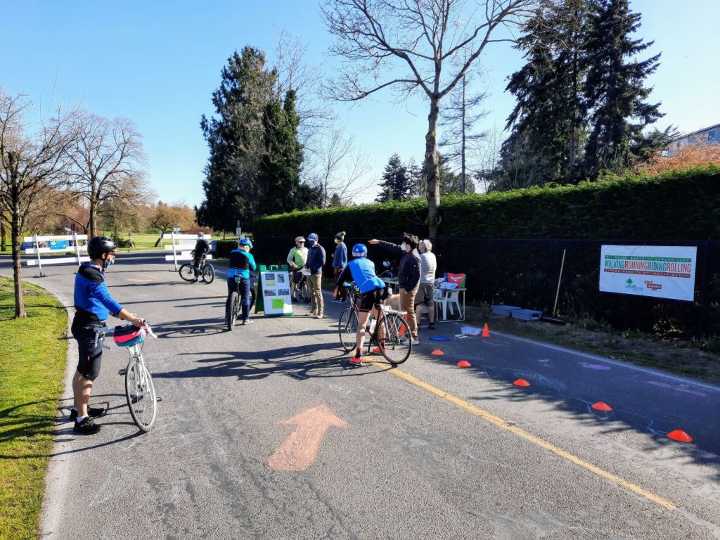 A group of bikers mostly in biking gear milling around a table while someone points