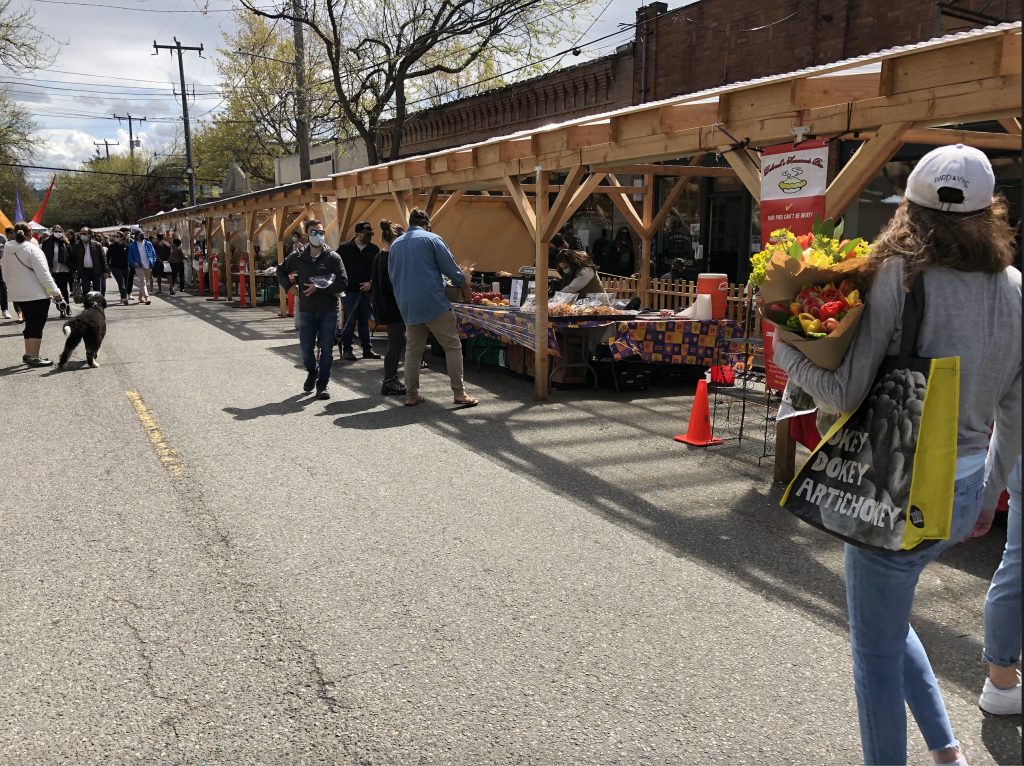 Wooden pergolas on Ballard Ave have farmers market booths set up in them. 