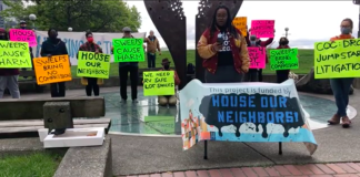 A photograph showing participants holding colorful signs at a press event. The signs carry messages such as "sweeps cause harm" and "sweeps bring no compassion"