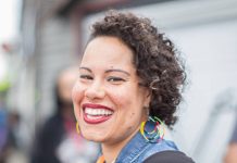 Nikkita Oliver Is Our Urbanist Meetup Guest on September 14th Nikkita is a Black woman. She wears rainbow hoop earrings. her curly hair to the side, and a big smile.