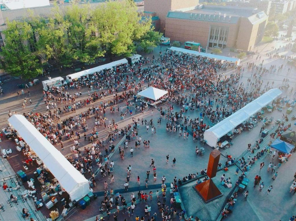 A busy UW Night Market in Red Square on the university campus. Vendor tents are located on the exterior of the square as pedestrians crowd the center area. 
