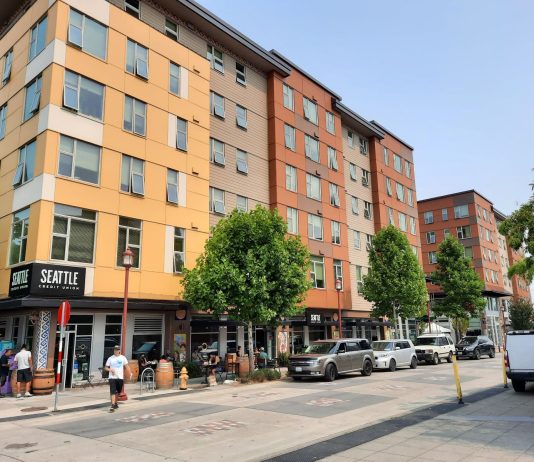 Social Housing Push Gaining Support as Housing Prices Skyrocket Image: A six story building with retail on the first level and pedestrians on the sidewalk.