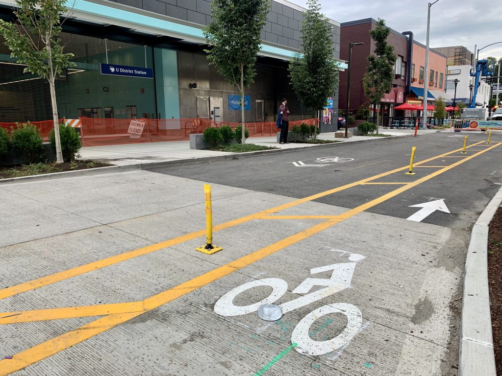 A photo of NE 43rd Street shows a protected bike lane leading to the U District station entrance. 