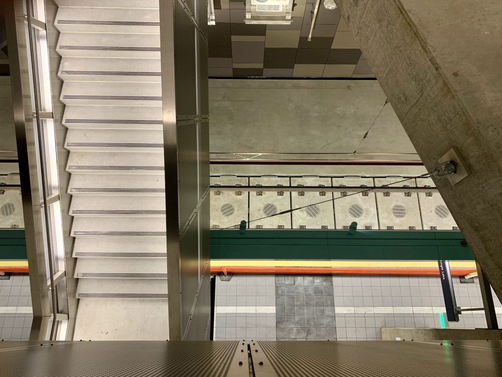 A photo shows the view of the stairs and light rail tracks looking down from an elevated platform. 