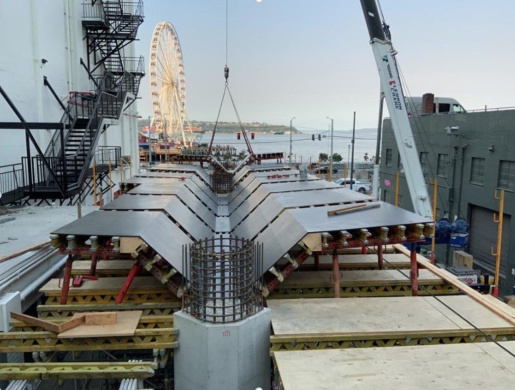 The metal support structure of the bridge is visible before the paved surface is installed. The Ferris wheel is visible in the background.