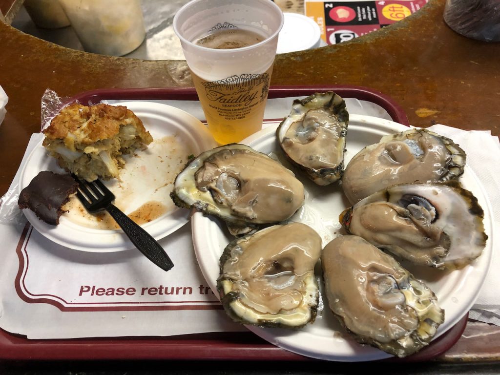A photo of a tray of food with a plate of oysters and crab cake on it.