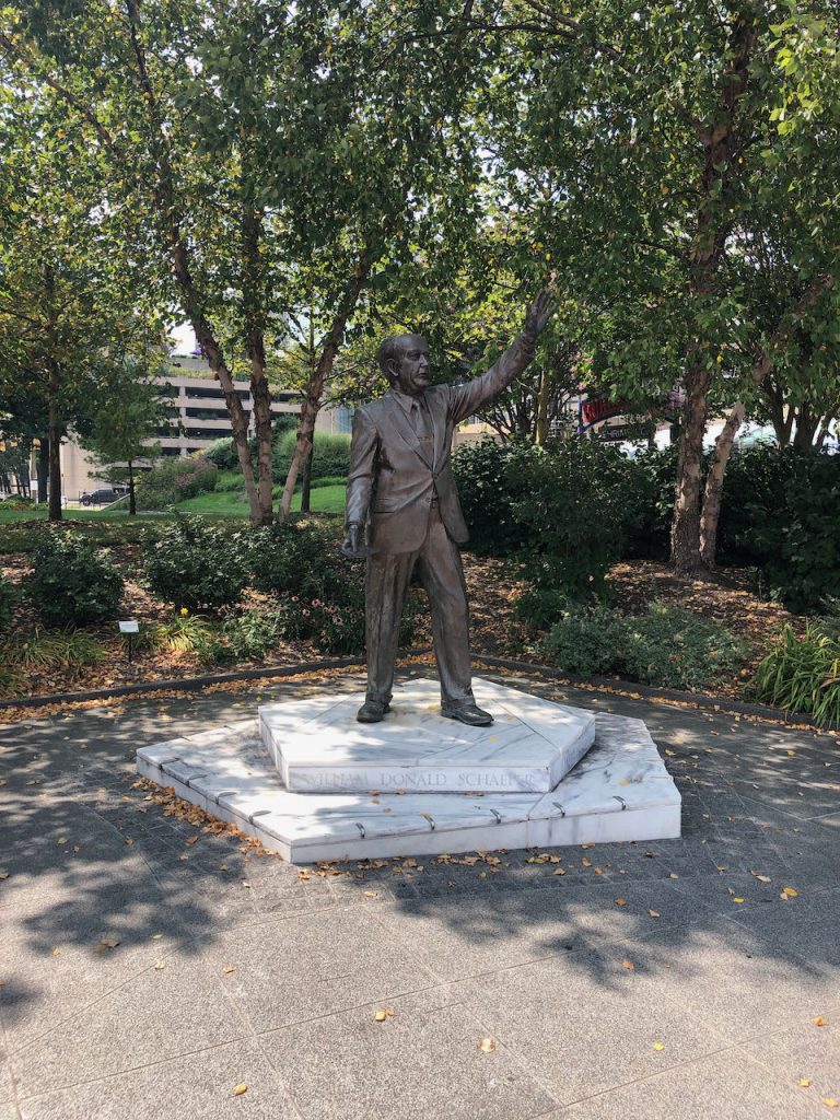 A photo a bronze statue of a man wearing a suit and raising his left arm. 
