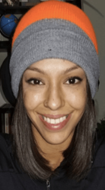 A brown skinned woman wearing an orange hat smiles at the camera.