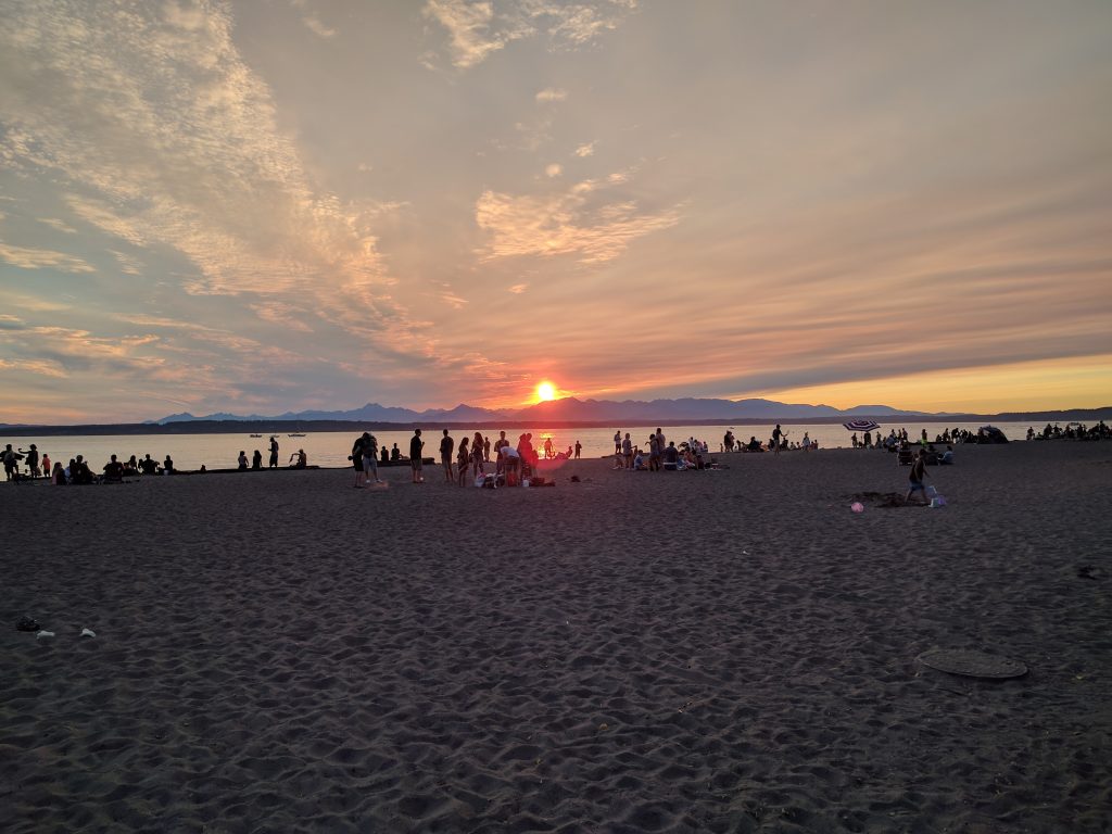 Golden Gardens at sunset. People are gathered at the beach, and the Olympic Mountains rounds out the sunset