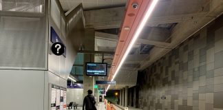 A photo of an underground light rail station platform. A man walks away from the camera. The train tracks are empty.