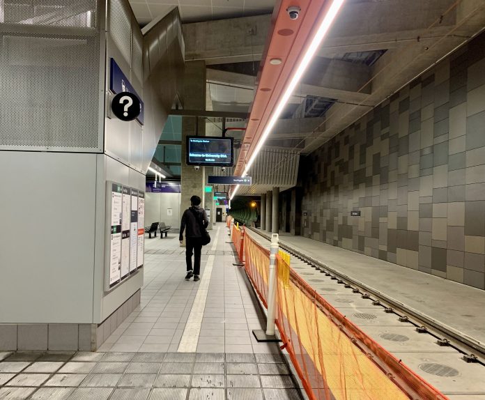 A photo of an underground light rail station platform. A man walks away from the camera. The train tracks are empty.