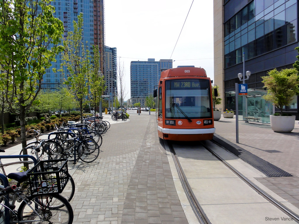 A photo of a streetcar in Portland with a large amount of parked bicycles nearby. 