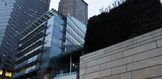 A photo of the Seattle City Hall with tall glass buildings illuminated at dusk in the background.
