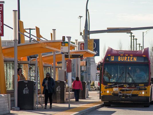 The Urbanist Podcast: Is Transit Back? A photo of people wait for an arriving King County Metro Bus at a RapidRide station.