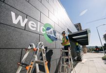 Celebrate Northgate Link Light Rail Expansion with Opening Day Events A photo of a worker standing on a ladder and stenciling welcome on to the exterior wall of the U District light rail station.