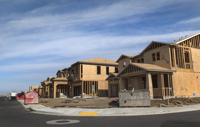 The photograph shows a curved street of a large two story houses with garages under construction