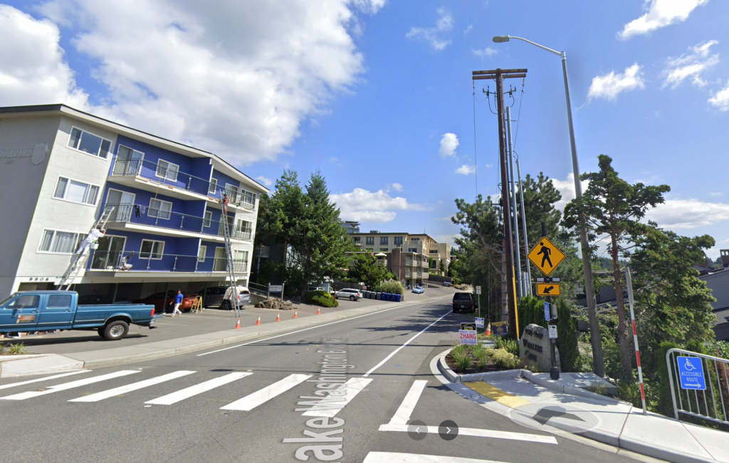 A photo of a wide residential street with a marked pedestrian crossing and an apartment building on the left side. 