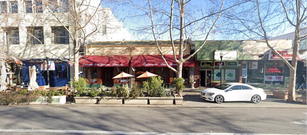 A view of a street with expanded cafe area in former parking spaces made permanent with cement planters.