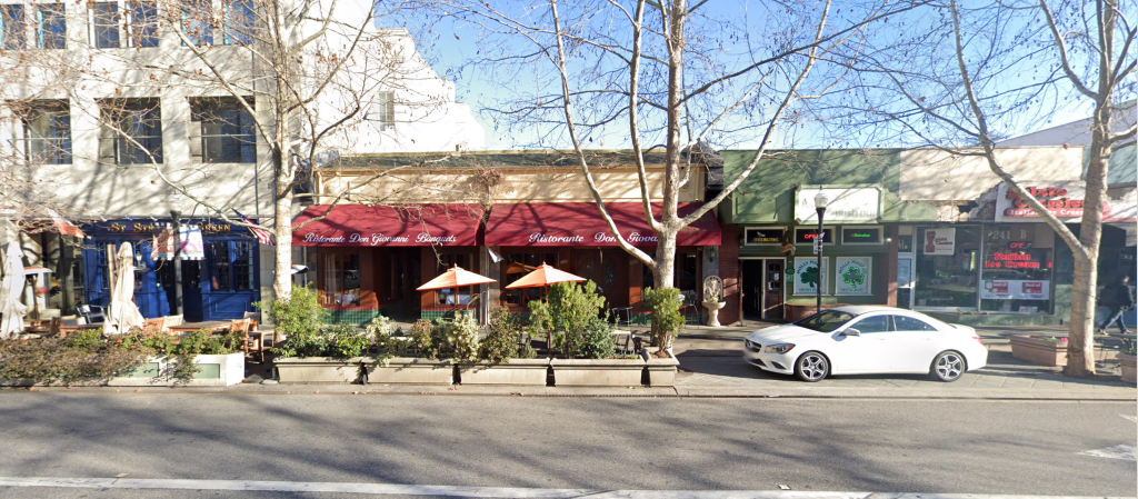 A view of a street with expanded cafe area in former parking spaces made permanent with cement planters. 