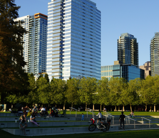 Improving Bellevue’s Grand Connection: Part 2 – Downtown Park to Bellevue Transit Center A photo of amphitheater style seating in a park with people sitting in the grass and tall modern buildings in the backdrop.