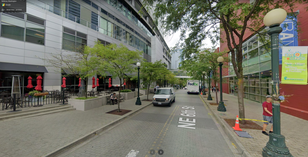 A photo of a narrow street flanked by wide sidewalks and commercial buildings. 